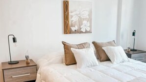 A bedroom with a bed, pillows, a nightstand, a lamp, a wall art piece, and a tiled floor. - Dpto ubicación ideal para 6 (Salta)