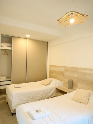 Een hotelkamer met twee bedden, een garderobe, een nachtkastje en een hanglamp.