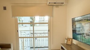 Un soggiorno moderno con un divano, una televisione, una lampada a sospensione in vimini e un'ampia finestra con vista sugli edifici.