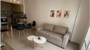 Een moderne woonkamer met een bank, twee ronde tafels en een keuken op de achtergrond.