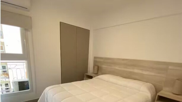 Een slaapkamer met een groot bed, een nachtkastje, een kledingkast en een raam.