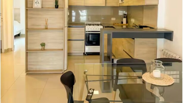 A modern kitchen with wooden cabinets, a glass dining table, and a built-in oven. - Dpto con excelente ubicación en Salta, Capital (Salta)