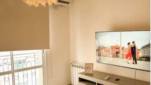 A modern living room with a large flat-screen TV, a decorative hanging light fixture, a balcony with metal railings, and a built-in entertainment unit. - Dpto con excelente ubicación en Salta, Capital (Salta)