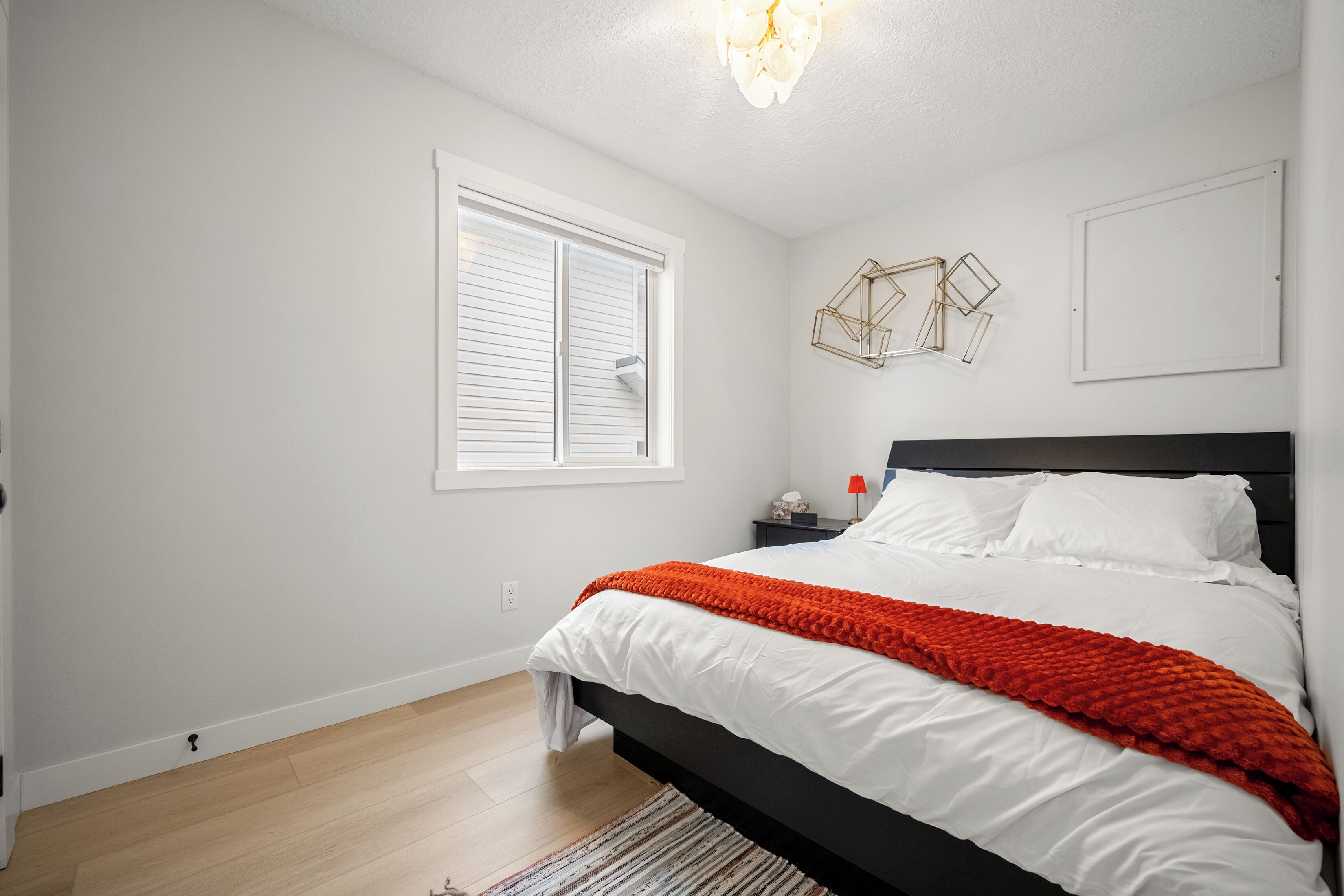 Quarto com cama, janela, mesa de cabeceira e luminária na parede.