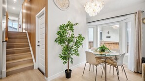Un intérieur moderne avec un escalier, un coin repas doté d’une table en verre et une plante en pot.