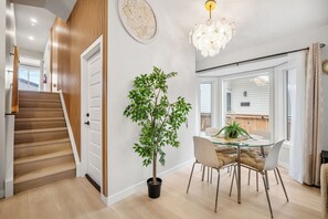 Un interior moderno con una escalera, una zona de comedor con mesa de vidrio y una planta en maceta.