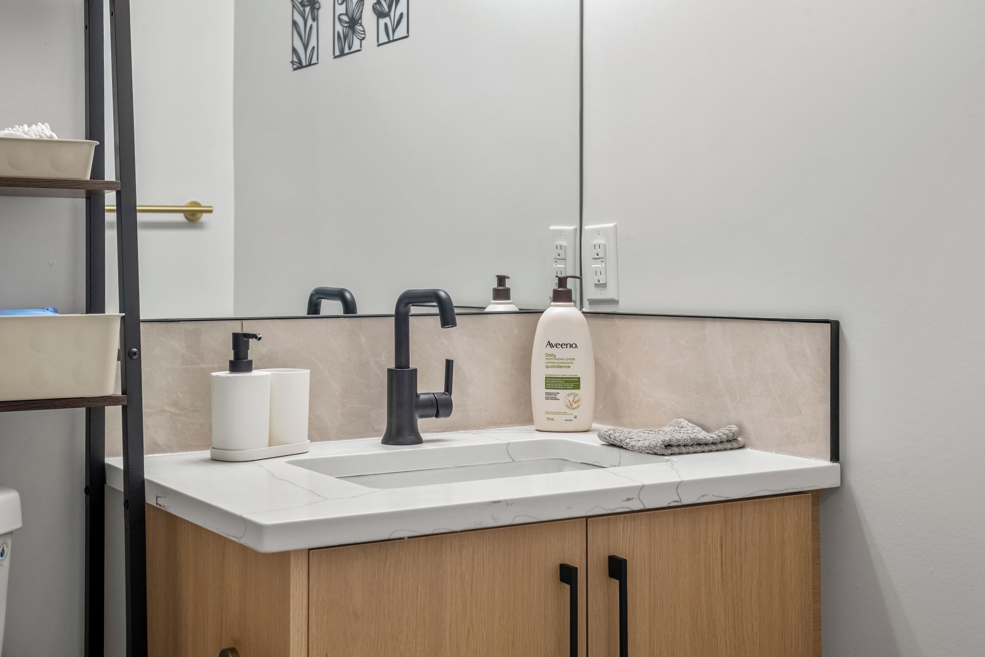 A bathroom with a white sink, black faucet, and a bottle of Aveeno shampoo.