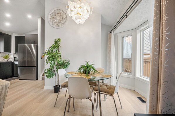 A modern kitchen with a stainless steel refrigerator, a dining table with chairs, and a potted plant.