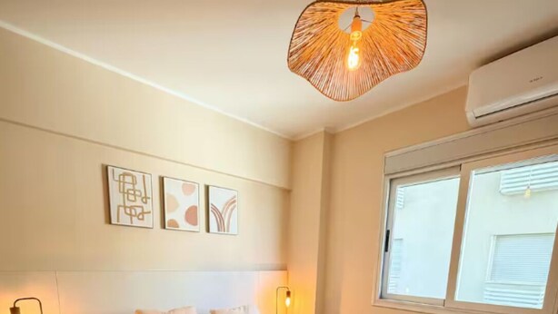 Ein Schlafzimmer mit einem großen Bett, Nachttischlampen, einer Deckenleuchte, einem Kunstwerk an der Wand und einem Fenster mit Jalousien.