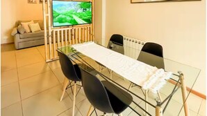 Ein moderner Essbereich mit einem Glastisch, schwarzen Stühlen, einem Fernseher und einer Holzwand.