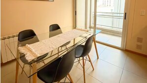 Ein Essbereich mit Glastisch, schwarzen Stühlen, einer gewebten Leuchte, einem Spiegel und einer Glasschiebetür zum Balkon.