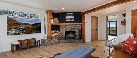 A spacious living room with a stone fireplace, wooden beams, a large painting, and a view through a glass door.