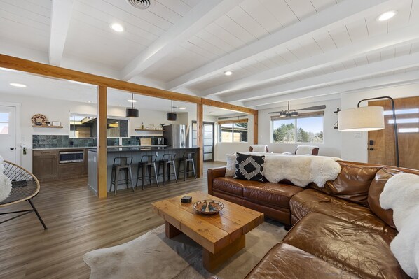 A spacious living area with a leather sofa, a wooden coffee table, and a kitchen in the background.