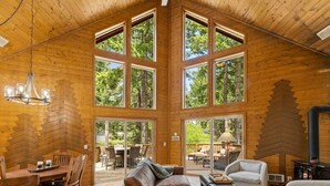 Eine geräumige Holzhütte mit hohen Decken, großen Fenstern, einem Kamin und einem Essbereich.