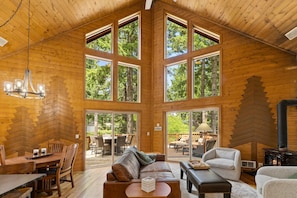 Eine geräumige Holzhütte mit hohen Decken, großen Fenstern, einem Kamin und einem Essbereich.