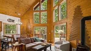 Eine geräumige Hütte mit hohen Decken, großen Fenstern, einem Kamin und einem Essbereich.