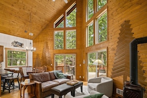 Eine geräumige Hütte mit hohen Decken, großen Fenstern, einem Kamin und einem Essbereich.