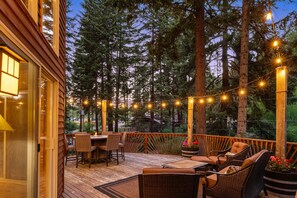 Eine Holterrasse mit Gartenmöbeln, Lichterketten und Blick auf hohe Bäume.