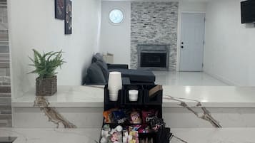 Una sala de estar moderna con chimenea, un sofá negro, una mesita de centro y una cesta de aperitivos.