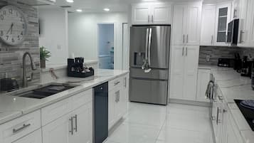 Una cocina moderna con gabinetes blancos, electrodomésticos de acero inoxidable, un reloj y luces empotradas en el techo.