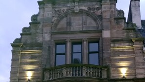 A historic building with a prominent entrance, large windows, and a balcony with railings.