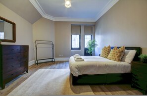 A bedroom with a bed, dresser, mirror, radiator, windows, and a plant. - Contractor Friendly 1-bed Ensuite Ayr Town Centre KA7 (Ayr)