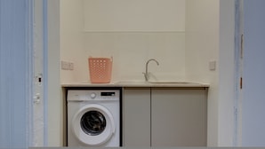 A compact laundry area with a washing machine, a sink, and a basket.