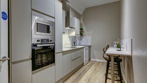 A compact kitchen with a microwave, oven, and dishwasher, a small dining area with a table and chairs, and a white door with a fire safety sign.