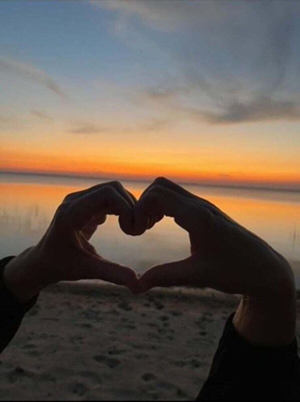 Une silhouette en forme de cœur, créée par des mains tendues, se découpant sur le ciel d’un coucher de soleil.