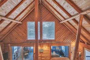 Ein Holzblockhaus-Interieur mit hohen Decken, Holzbalken und großen Fenstern.
