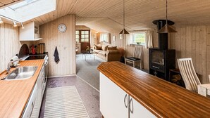 Interior de madera con cocina, comedor y sala de estar, que incluye estufa, sofá y un reloj.