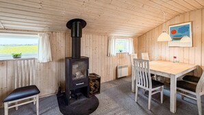 Una habitación acogedora con una estufa de leña, una mesa de comedor con sillas y vistas al exterior.