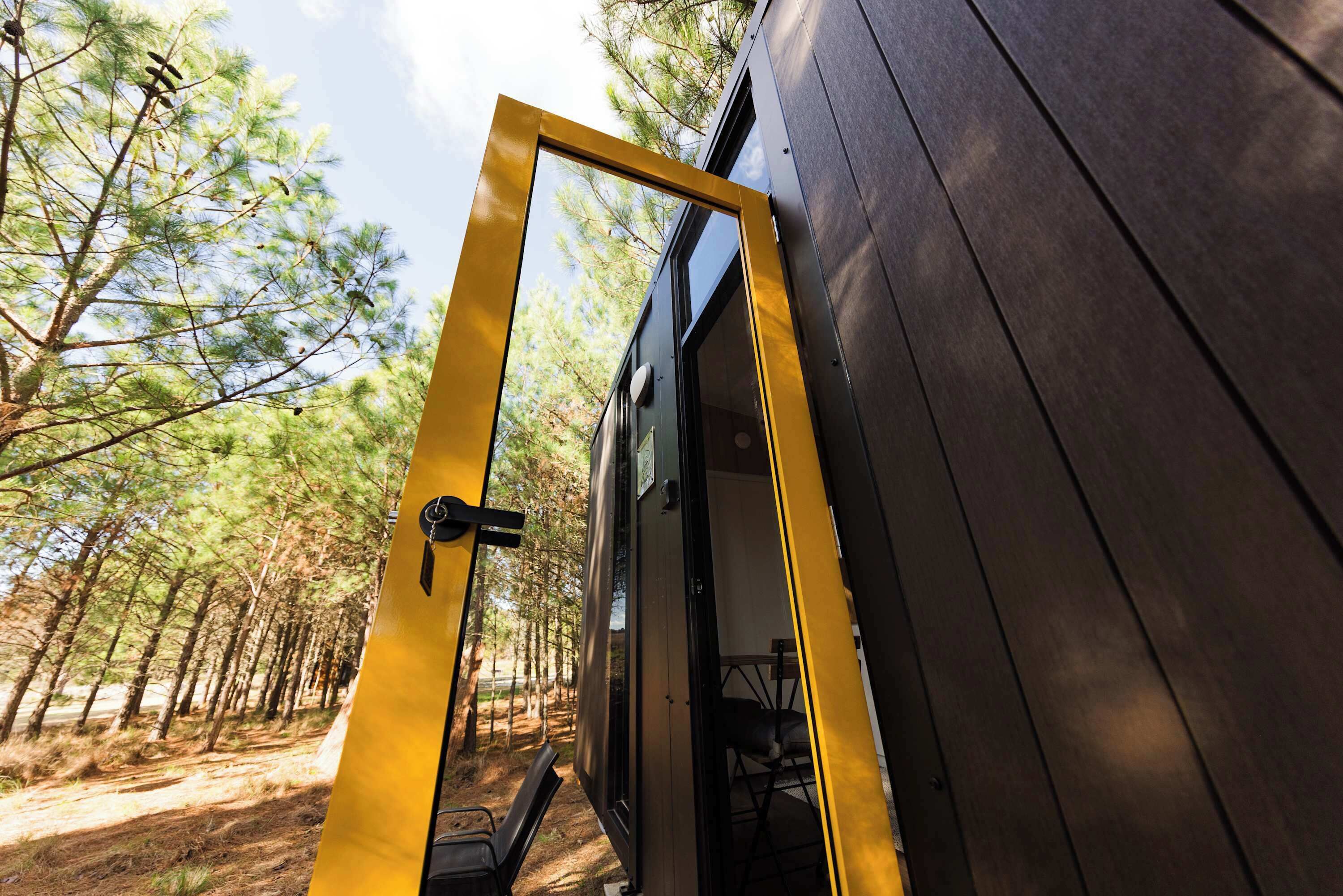 A wooden door with a yellow frame leading to an outdoor area with trees.