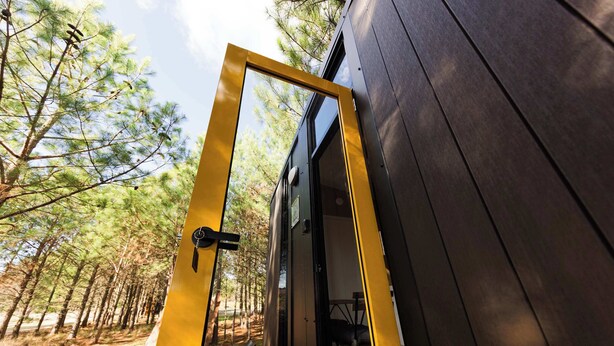 A wooden door with a yellow frame leading to an outdoor area with trees.