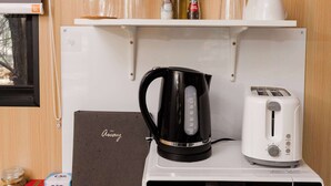 A kitchenette with a microwave, toaster, kettle, and shelves with glassware and condiments.