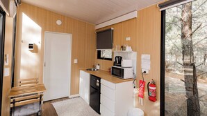 A compact kitchen with a sink, microwave, and a small refrigerator. There is a bench with cushions and a fire extinguisher mounted on the wall.