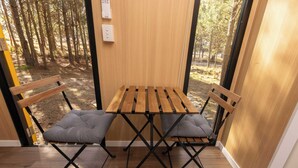 A wooden table with two chairs, a bench, and a view of a forest through a glass door.