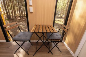 A wooden table with two chairs, a bench, and a view of a forest through a glass door.