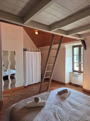 Ein Schlafzimmer mit erhöhtem Schlafbereich, einer Leiter, einem Fenster und einer Heizung.