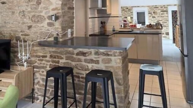 Uma cozinha moderna com parede de pedra, uma ilha central com banquetas e uma televisão à esquerda.