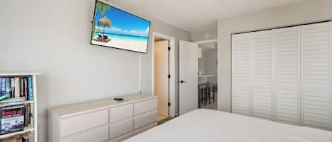 Une chambre à coucher avec un lit, un téléviseur fixé au mur, une bibliothèque et un placard.