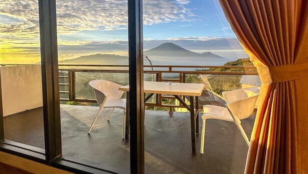 A balcony with a table and chairs, overlooking a mountainous landscape with a clear sky. - Cabin Athenea Sikapuk (Kejajar)
