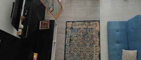 Una habitación con un sofá azul, un tapete estampado, un espejo y cortinas blancas.