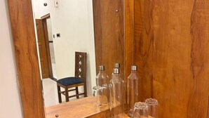 A wooden vanity with a mirror, clear glass bottles, and a chair. - Thamira Grand Palace (Nagercoil)