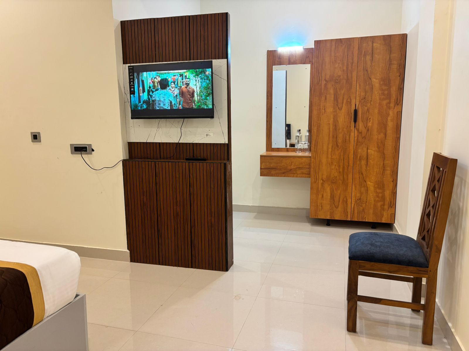 Ein Hotelzimmer mit einem Bett, einem an einer Holzplatte montierten Fernseher, einem Holzschrank, einem Spiegel und einem Sessel.