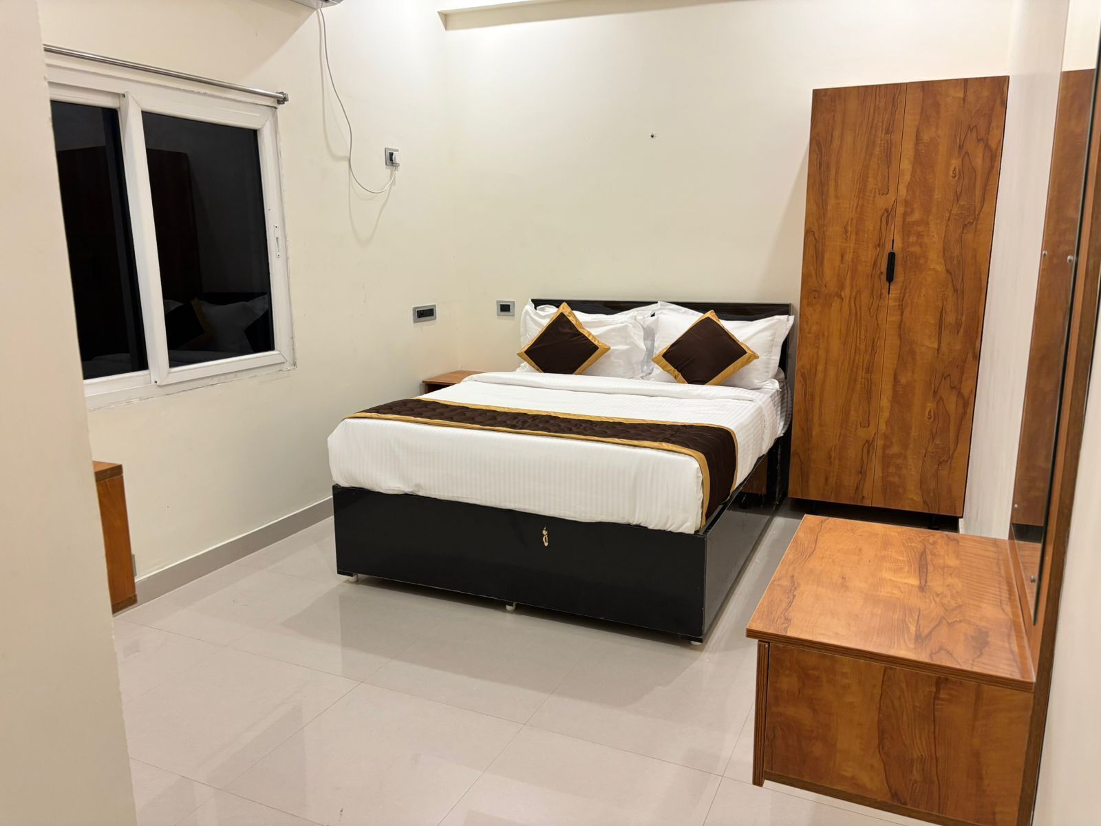Un dormitorio con cama, un armario de madera, una ventana y una mesita de madera.