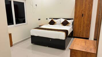 Un dormitorio con cama, un armario de madera, una ventana y una mesita de madera.