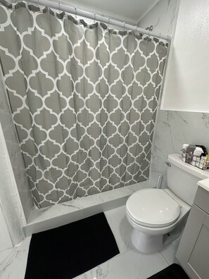 A bathroom with a patterned shower curtain, a toilet, a sink, and a marble floor.