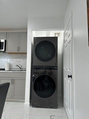 A compact laundry room with a front-loading washer and dryer, a microwave, and a tiled backsplash.