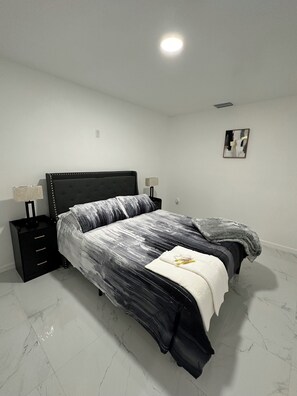 Un dormitorio con cama, mesitas de noche, una lámpara de pared y una luz en el techo.